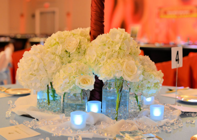 Blue tablecloth with white florals, votives, and jewel centerpiece at a Fire and Ice themed charity fundraiser event in Ocala, Florida.