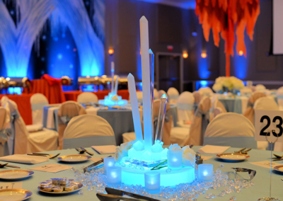 Blue tablecloth with acrylic lighted ice sculpture, votives, and jewel centerpiece at a Fire and Ice themed charity fundraiser event in Ocala, Florida.